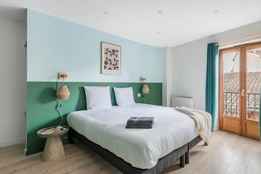 La chambre aux murs vert sauge, avec son lit king size et sa fenêtre sur les toits